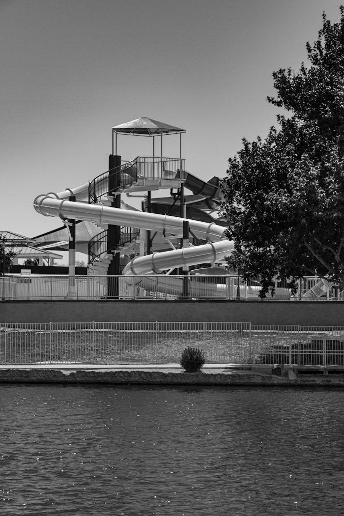 Serene black and white photo of a waterpark slide beside a tranquil lake.